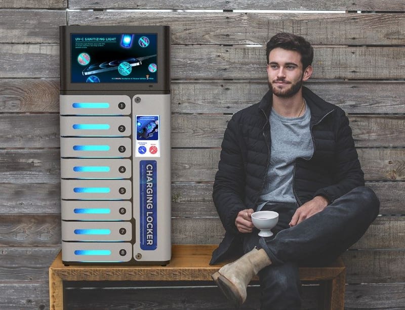 A freestanding charging locker in a lounge, with a person seated on a bench beside it