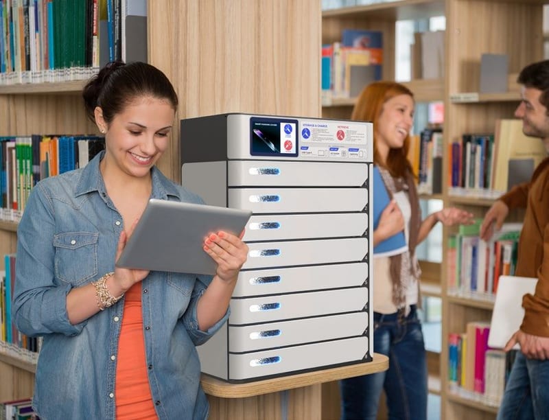 Students at a stack of device charging lockers between library shelving
