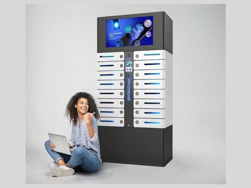 A freestanding charging locker with a large portrait display above the bays, standing against a plain wall